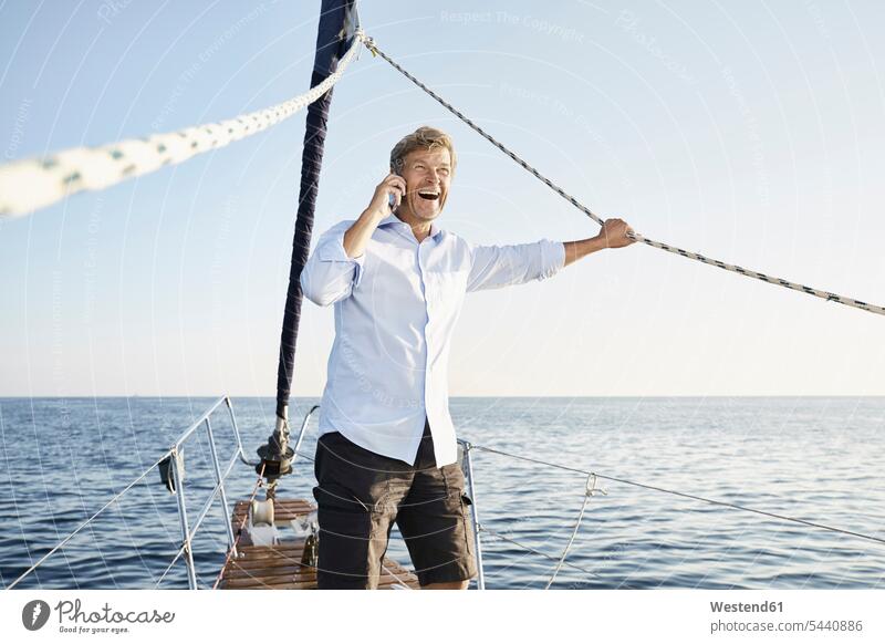 Lachender reifer Mann am Telefon auf seinem Segelboot Segeln segelnd segelt Männer männlich Bootsport Erwachsener erwachsen Mensch Menschen Leute People