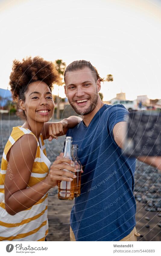 Zwei Freunde mit Bierflaschen machen ein Selfie am Strand Beach Straende Strände Beaches Selfies Portrait Porträts Portraits Freundschaft Kameradschaft Abend