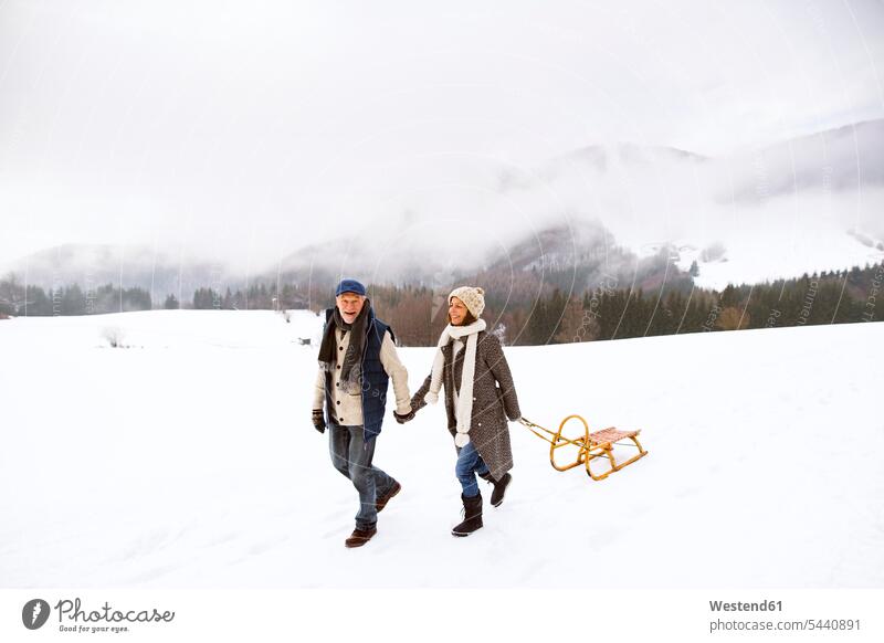 Glückliches älteres Ehepaar beim Schlittenfahren in schneebedeckter Landschaft Seniorenpaar älteres Paar Seniorenpaare ältere Paare Seniorenpärchen