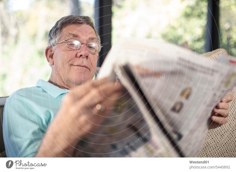 Älterer Mann sitzt auf Couch und liest Zeitung Männer männlich Zeitungen sitzen sitzend lesen Lektüre Sofa Couches Liege Sofas Zuhause zu Hause daheim Senior