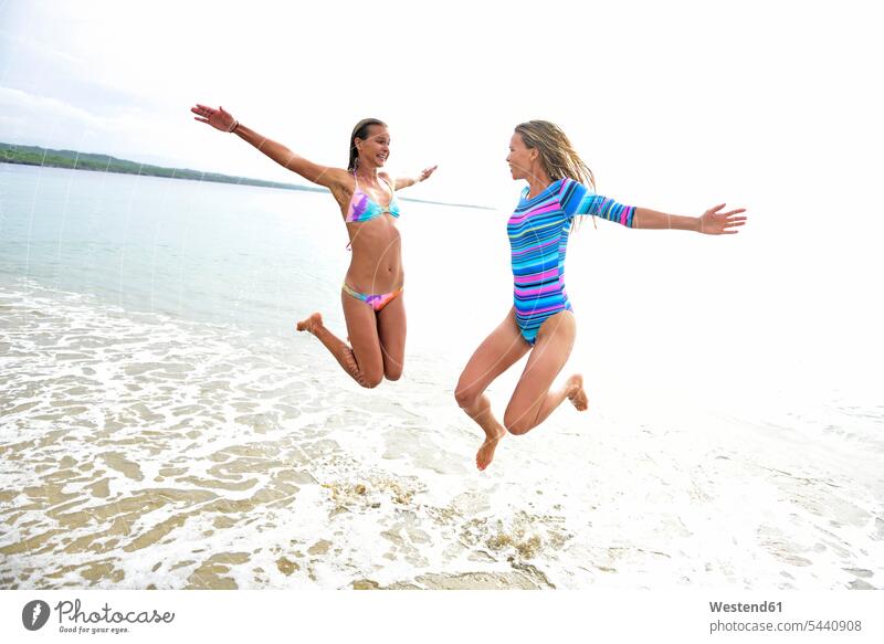 Zwei Frauen amüsieren sich am Strand Freundinnen springen hüpfen Beach Straende Strände Beaches Spaß Spass Späße spassig Spässe spaßig weiblich Freunde