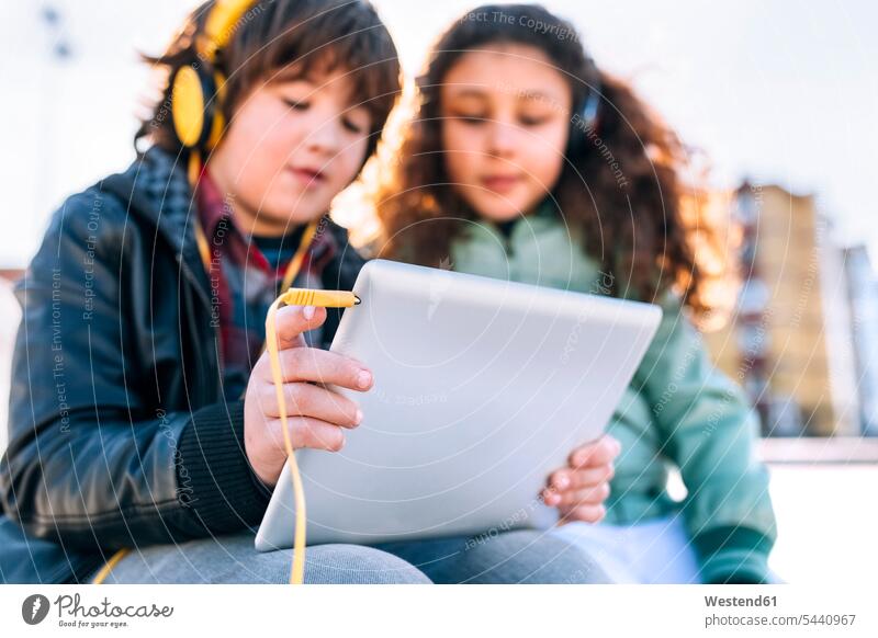 Zwei Kinder, die mit Kopfhörer und Tablett Musik hören Tablet Computer Tablet-PC Tablet PC iPad Tablet-Computer Rechner sitzen sitzend sitzt benutzen benützen