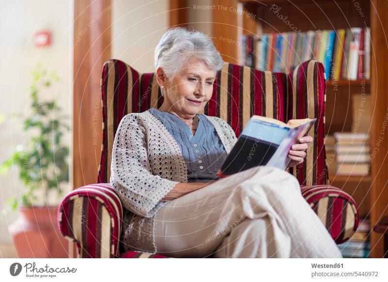 Ältere Frau sitzt in Bibliothek, liest Buch sitzen sitzend lesen Lektüre Sessel Altersheim Altenheim Seniorenheim Bücher Seniorin älter Seniorinnen alt Stuhl