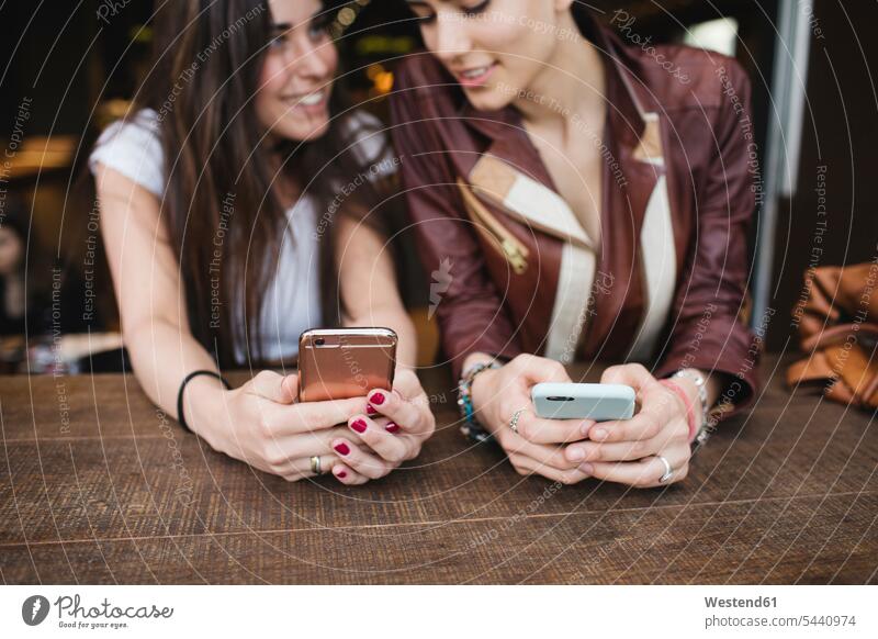 Zwei junge Frauen benutzen Mobiltelefone in einer Bar lächeln Freundinnen Handy Handies Handys Freunde Freundschaft Kameradschaft Telefon telefonieren