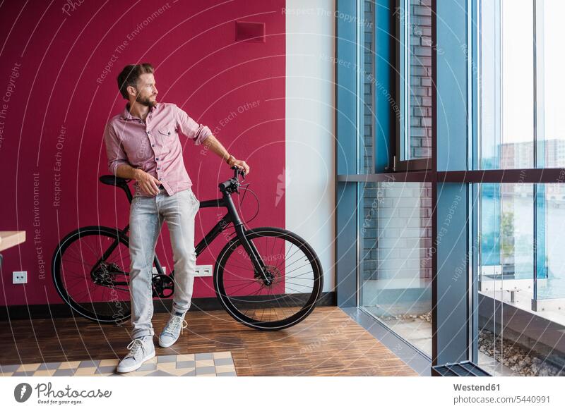 Mann mit Fahrrad steht im modernen Büro und schaut aus dem Fenster Bikes Fahrräder Räder Rad Männer männlich Raeder Erwachsener erwachsen Mensch Menschen Leute