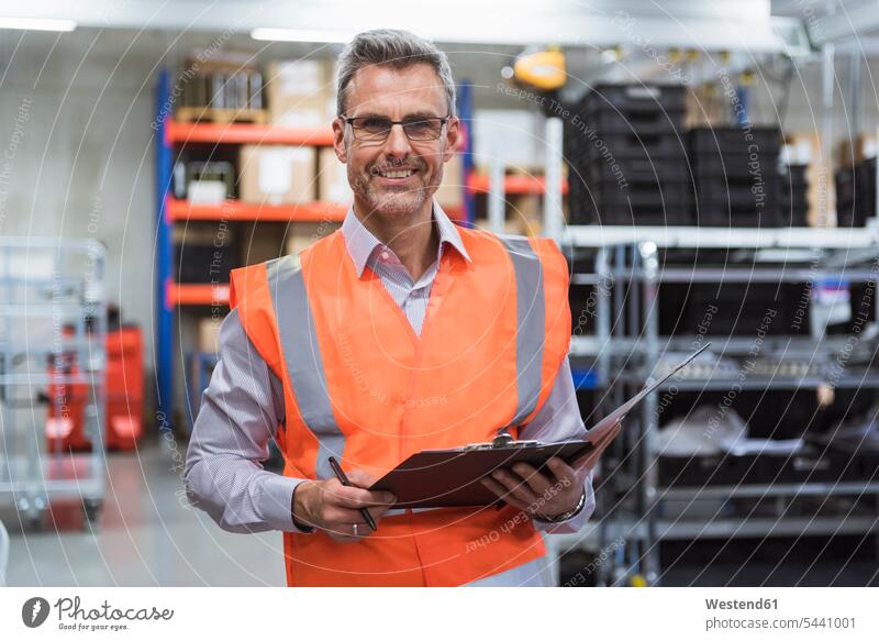 Porträt eines lächelnden Mannes in der Fabrikhalle, der eine Sicherheitsweste trägt und ein Klemmbrett hält arbeiten Arbeit prüfen Kontrolle Untersuchung