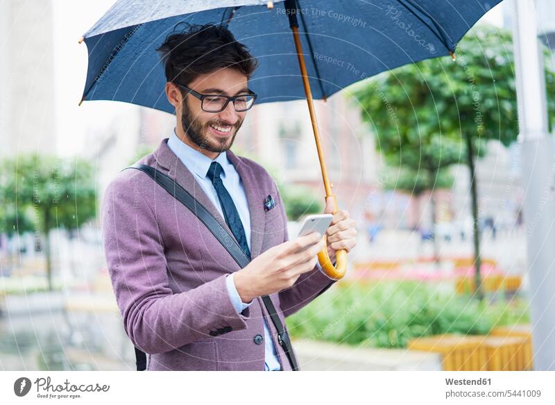 Modischer Geschäftsmann mit Regenschirm, der sein Handy in der Stadt überprüft modisch checken Businessmann Businessmänner Geschäftsmänner Mann Männer männlich