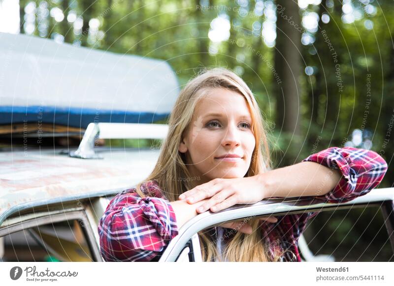 Lächelnde junge Frau beim Auto im Wald Wagen PKWs Automobil Autos lächeln Forst Wälder weiblich Frauen Kraftfahrzeug Verkehrsmittel KFZ Erwachsener erwachsen