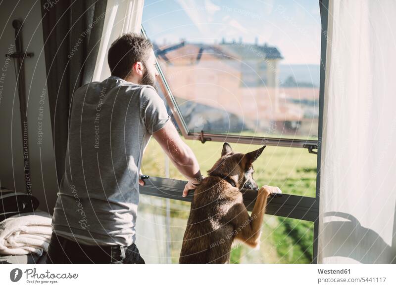 Junger Mann steht mit seinem Hund am Fenster und wartet jung stehen stehend Hunde Zuhause zu Hause daheim warten Männer männlich Haustier Haustiere Tier