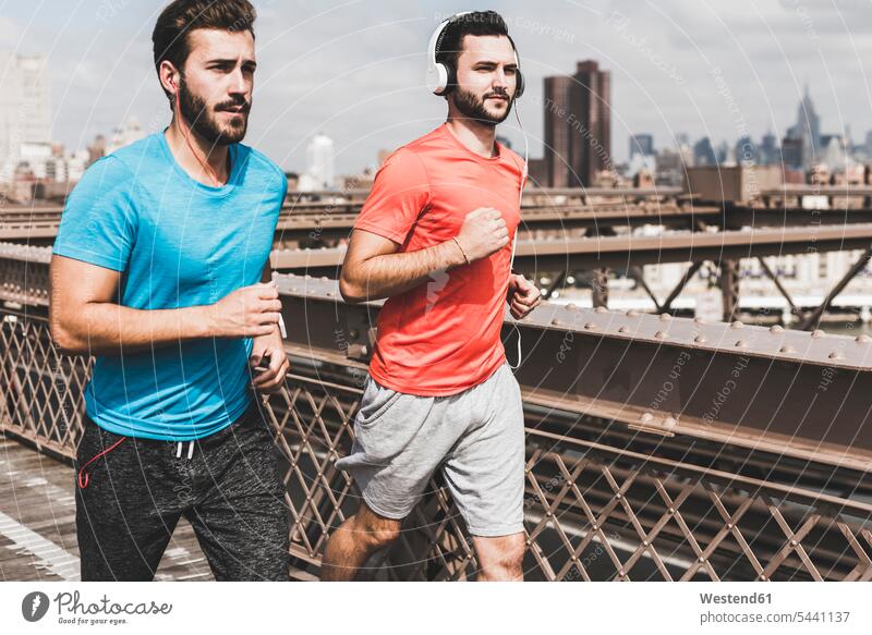 USA, New York City, zwei Männer laufen auf der Brooklyn Brige Joggen Jogging Mann männlich Brücke Bruecken Brücken rennen Kopfhörer Kopfhoerer Fitness fit