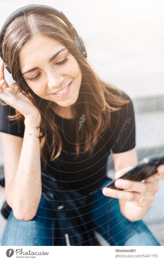 Lächelnde junge Frau, die im Freien Musik hört Kopfhörer Kopfhoerer hören hoeren lächeln weiblich Frauen Erwachsener erwachsen Mensch Menschen Leute People