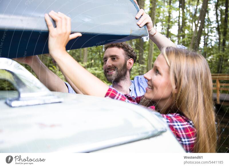 Lächelndes junges Paar nimmt Kanu vom Autodach Kanus Wald Forst Wälder Pärchen Paare Partnerschaft nehmen aufnehmen Wagen PKWs Automobil Autos lächeln