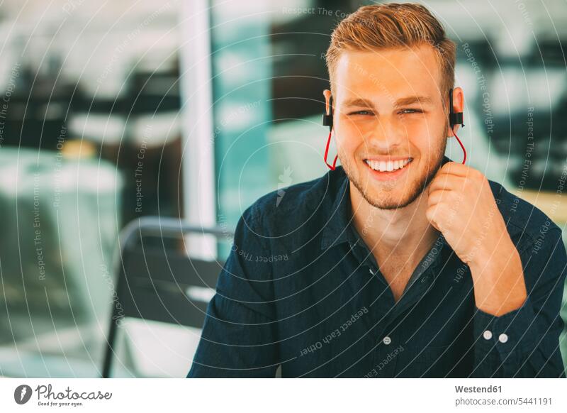 Junger Mann trägt Kopfhörer im Freien Ohrhörer Männer männlich Kopfhoerer In-Ear Erwachsener erwachsen Mensch Menschen Leute People Personen Musik lächeln hören