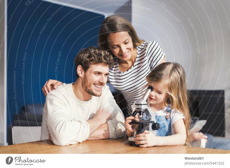 Eltern beobachten Tochter bei der Benutzung eines Mikroskops und lächeln stolz spielen clever schlau Mädchen weiblich Mikroskope Vater Papas Väter Vati Vatis