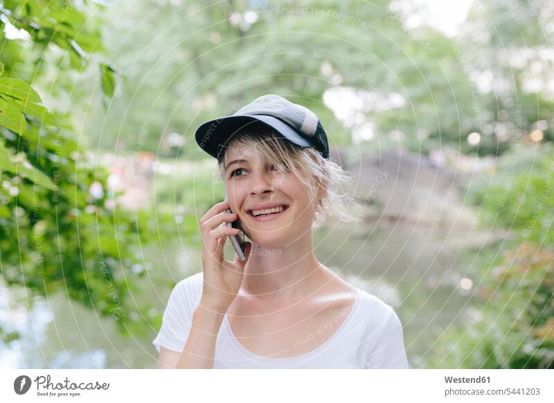 Lächelnde junge Frau im Park beim Telefonieren mit dem Handy Parkanlagen Parks Mobiltelefon Handies Handys Mobiltelefone lächeln telefonieren anrufen Anruf