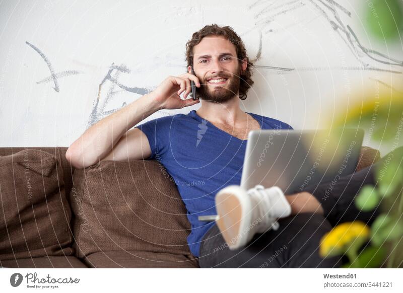 Porträt eines jungen Mannes am Telefon, der in einem Café auf der Couch sitzt Männer männlich Portrait Porträts Portraits telefonieren anrufen Anruf