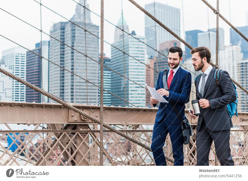 USA, New York City, zwei Geschäftsleute diskutieren über ein Dokument zur Brooklyn Bridge sprechen reden New York State Brücke Bruecken Brücken Geschäftsmann