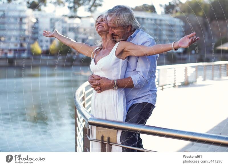 Älteres Ehepaar macht eine Städtereise, umarmt sich an einem Geländer unterwegs auf Achse in Bewegung liebevoll zaertlich einfühlsam einfuehlsam zärtlich sanft