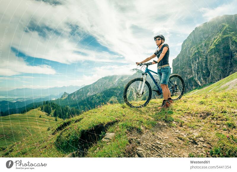 Deutschland, Bayern, Pfronten, Frau mit Mountainbike auf Almwiese bei Aggenstein Aussicht Ausblick Ansicht Überblick Mountainbikes weiblich Frauen stehen