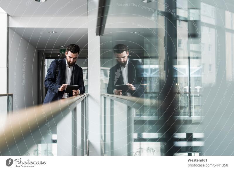 Geschäftsmann steht im Bürogebäude und benutzt ein digitales Tablet Geländer Brüstung Balustrade unterwegs auf Achse in Bewegung differenzierter Fokus