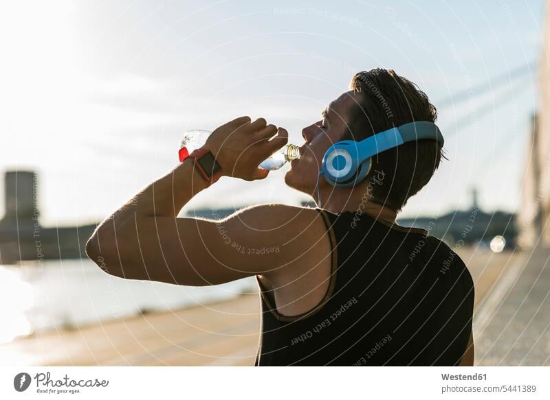 Junger Mann mit Kopfhörern, Trinkwasser sportlich Jogger Wasser Musik Männer männlich Sportler fit trainieren trinken Joggen Jogging Fitness Gesundheit gesund