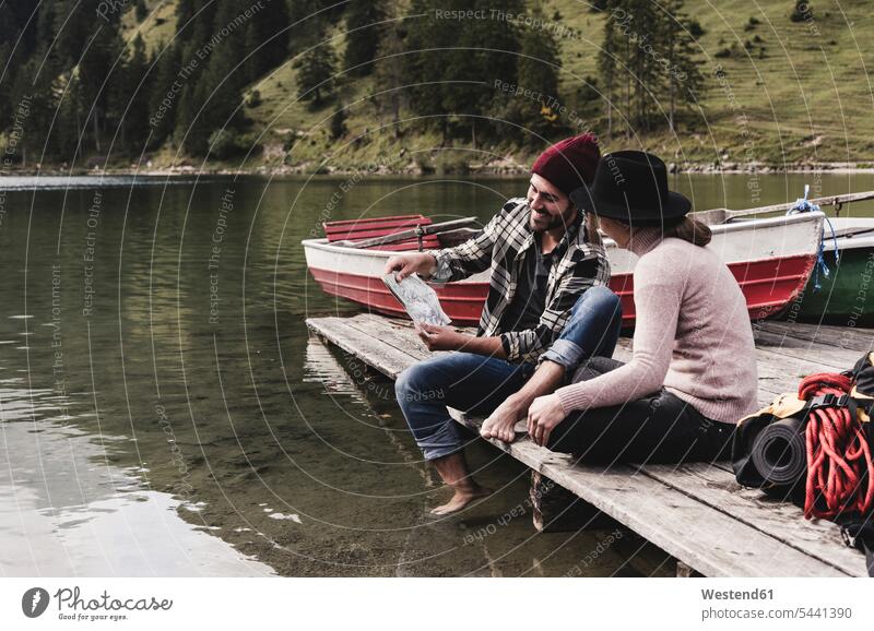 Österreich, Tirol, Alpen, Ehepaar mit Karte auf Steg am Bergsee sitzend See Seen Paar Pärchen Paare Partnerschaft lächeln Gewässer Wasser Mensch Menschen Leute