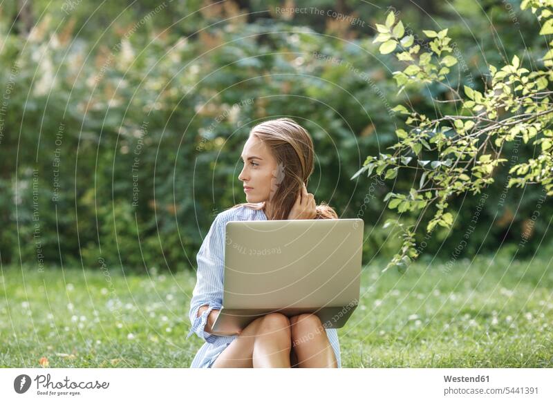 Junge Frau mit Laptop auf einer Wiese mit seitlichem Blick Park Parkanlagen Parks Notebook Laptops Notebooks weiblich Frauen Computer Rechner Erwachsener