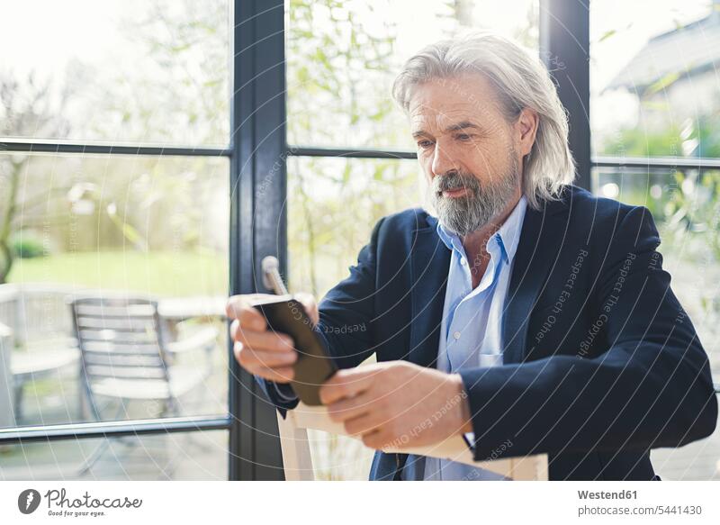 Leitender Geschäftsmann sitzt auf einem Stuhl und benutzt ein Smartphone Mann Männer männlich Handy Mobiltelefon Handies Handys Mobiltelefone lesen Lektüre SMS