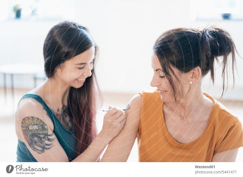 Frau malt Tätowierung auf den Arm einer anderen Frau lächeln Tattoo Tätowierungen Tatoos Taetowierung Tattoos Taetowierungen weiblich Frauen tätowiert