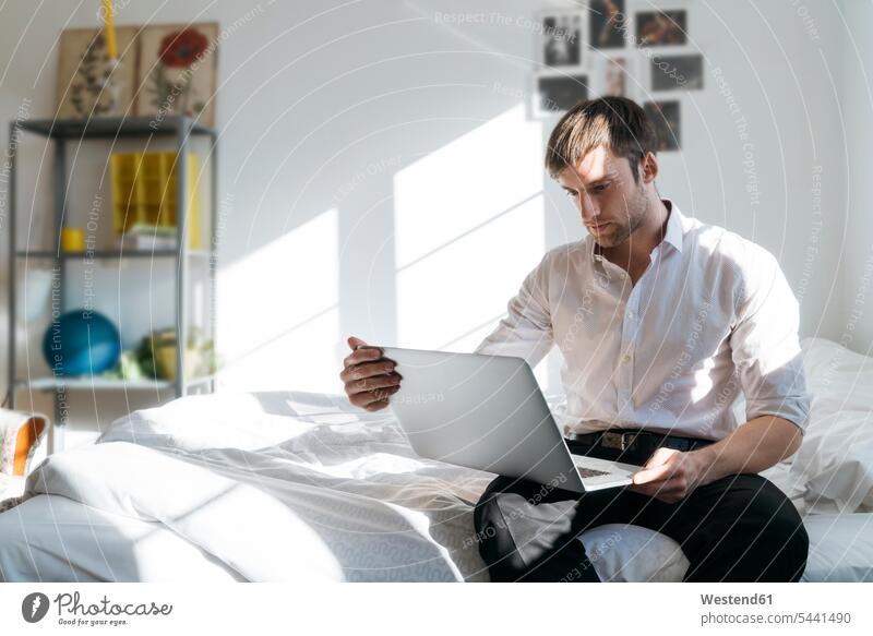 Junger Mann sitzt mit Laptop im Bett Notebook Laptops Notebooks Männer männlich Betten Computer Rechner Erwachsener erwachsen Mensch Menschen Leute People
