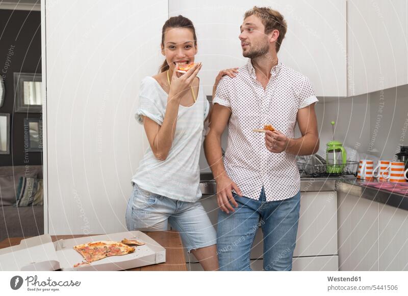 Junges Paar isst Pizza in der Küche Pizzen Küchen Pärchen Paare Partnerschaft essen essend Essen Food Food and Drink Lebensmittel Essen und Trinken