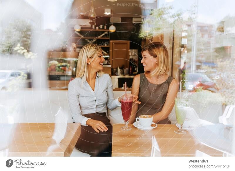 Zwei glückliche junge Frauen in einem Cafe Spaß Spass Späße spassig Spässe spaßig sprechen reden Kaffeehaus Bistro Cafes Café Cafés Kaffeehäuser lächeln