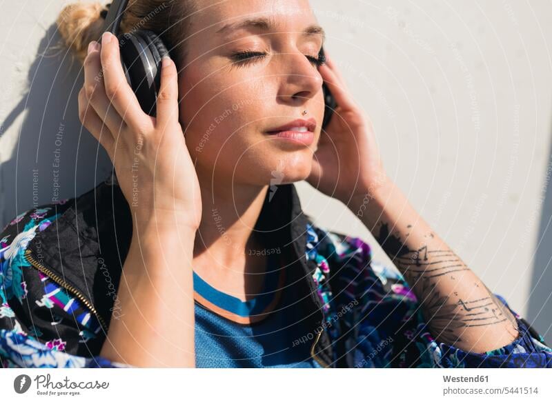 Porträt einer jungen Frau mit geschlossenen Augen, die mit Kopfhörern Musik hört weiblich Frauen Kopfhoerer Portrait Porträts Portraits Erwachsener erwachsen