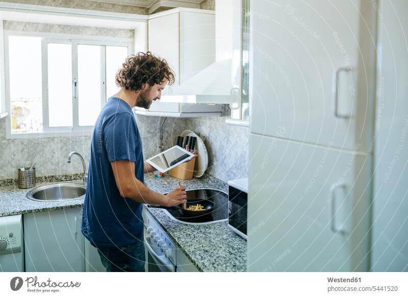 Mann kocht in Küche, während er auf Tablette schaut Tablet Computer Tablet-PC Tablet PC iPad Tablet-Computer Küchen kochen Männer männlich Rechner Erwachsener