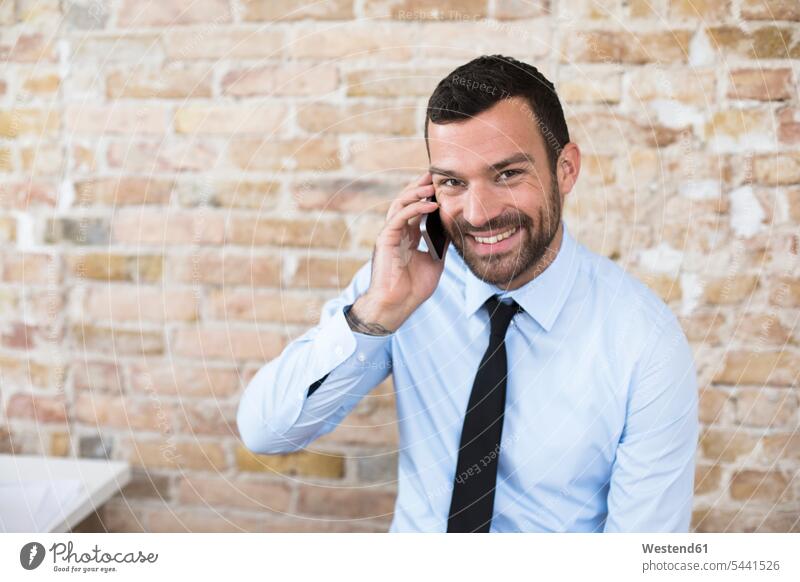 Porträt eines lächelnden Geschäftsmannes am Telefon an der Ziegelmauer Backsteinwand Backsteinmauern telefonieren anrufen Anruf telephonieren Handy Mobiltelefon