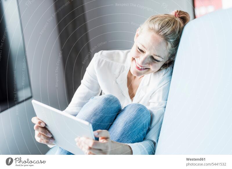 Lächelnde Frau sitzt auf Couch und benutzt Tablette lächeln weiblich Frauen Tablet Computer Tablet-PC Tablet PC iPad Tablet-Computer sitzen sitzend Erwachsener