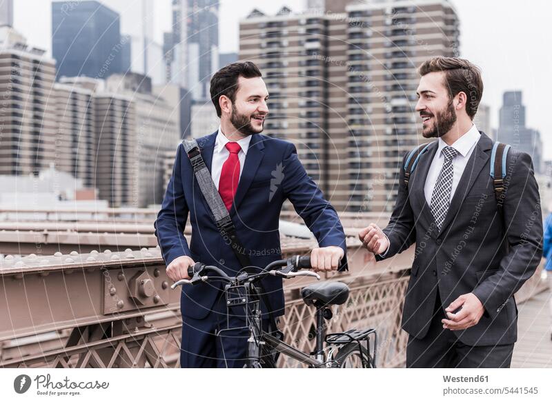 USA, New York City, zwei Geschäftsleute mit Fahrrad auf der Brooklyn Bridge sprechen reden Brücke Bruecken Brücken lächeln Geschäftsmann Businessmann