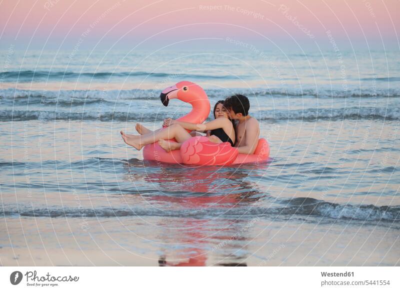 Verliebtes Paar schwebt mit aufblasbarem rosa Flamingo bei Sonnenuntergang auf dem Meer Pärchen Paare Partnerschaft Meere Mensch Menschen Leute People Personen
