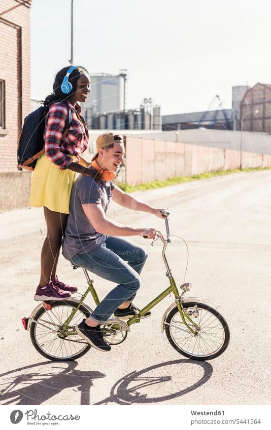 Junges Paar fährt Fahrrad mit einem Mädchen auf einem Gepäckträger stehend radfahren fahrradfahren radeln multikulturell steht aktiv fröhlich Fröhlichkeit