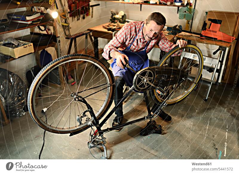 Älterer Mann überprüft Fahrrad in seiner Werkstatt Senior ältere Männer älterer Mann Senioren Bikes Fahrräder Räder Rad Werkstätte Werkstaette Werkstaetten