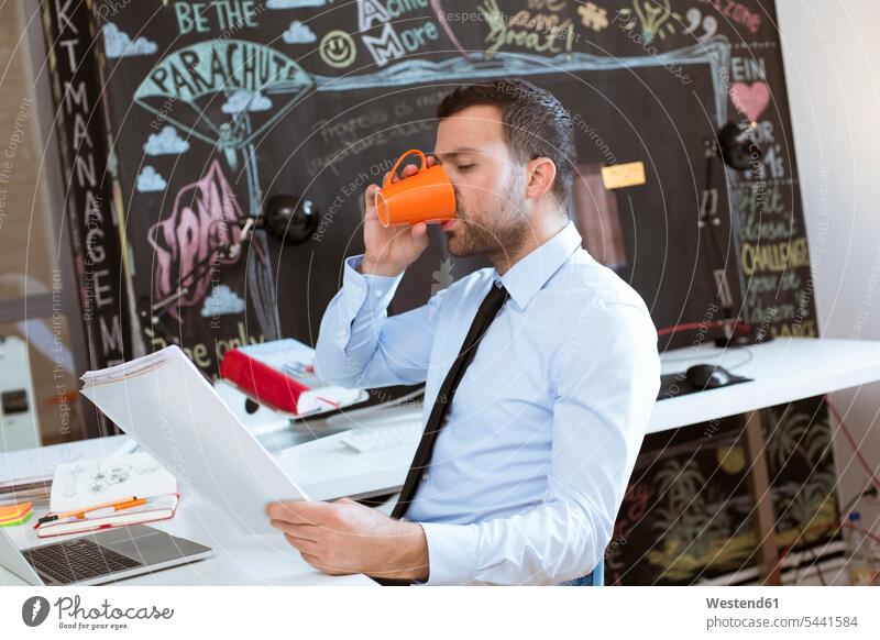 Geschäftsmann im Kreativbüro, der sich Dokumente ansieht und Kaffee trinkt trinken Businessmann Businessmänner Geschäftsmänner lesen Lektüre Getränk Getraenk