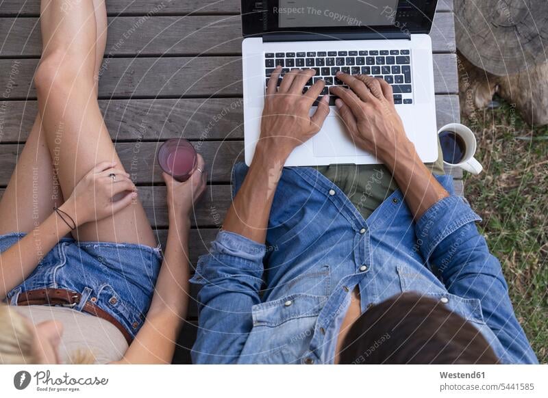Draufsicht eines Mannes, der auf der Terrasse sitzt und einen Laptop neben einer Frau benutzt Terrassen Notebook Laptops Notebooks Paar Pärchen Paare