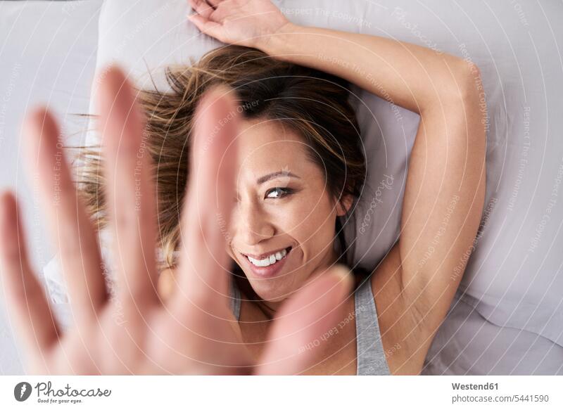 Porträt einer lächelnden Frau, die im Bett liegt und ihre Hand hebt Betten Gesicht Gesichter Portrait Porträts Portraits Hände liegen liegend weiblich Frauen