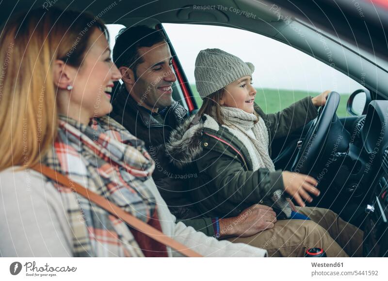Glückliche Familie im Auto mit einem kleinen Mädchen auf dem Schoß des Vaters, das vorgibt zu fahren Wagen PKWs Automobil Autos fahrend fahrender fahrendes
