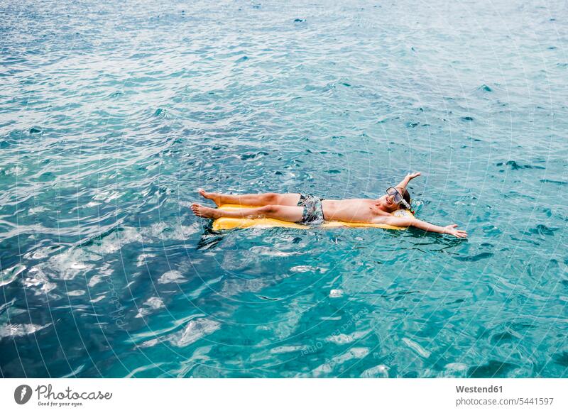 Glücklicher junger Mann entspannt sich auf dem Luftbett im Meer Meere Luftmatratze Luftmatratzen Gewässer Wasser Urlaub Ferien liegen liegend liegt genießen