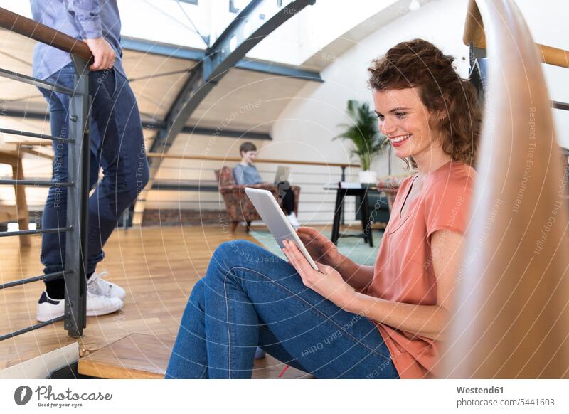 Lächelnde Frau sitzt in modernem Büro mit Tablett auf dem Boden sitzen sitzend Kollegen Arbeitskollegen Tablet Computer Tablet-PC Tablet PC iPad Tablet-Computer