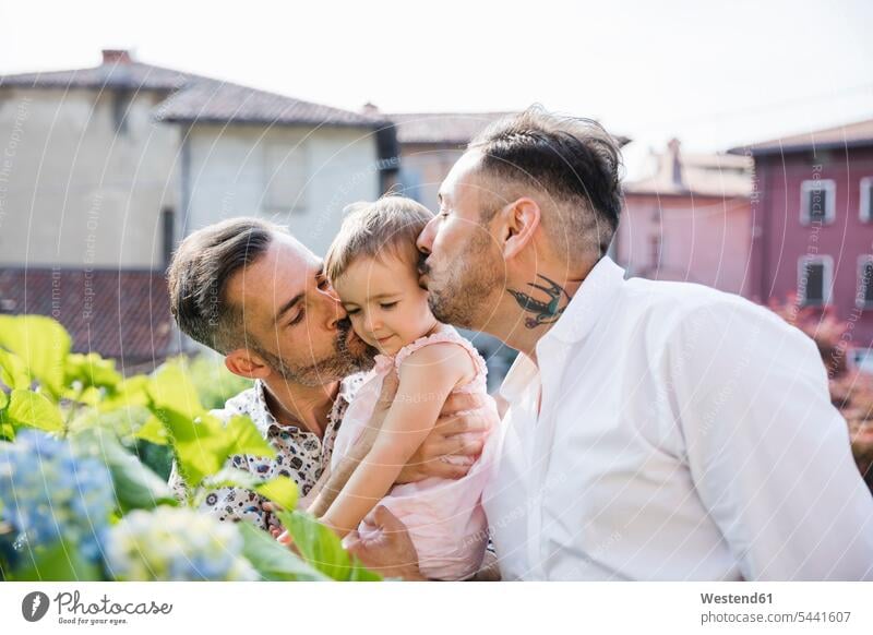 Schwules Paar küsst ihre Tochter im Garten Töchter küssen Küsse Kuss Pärchen Paare Partnerschaft schwul Homosexueller Mann Homosexuelle Maenner Schwuler