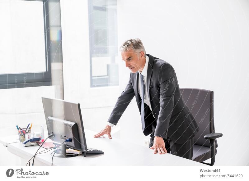 Ein reifer Geschäftsmann steht im Büro und schaut auf den Computer Businessmann Businessmänner Geschäftsmänner stehen stehend Manager Office Büros Verantwortung