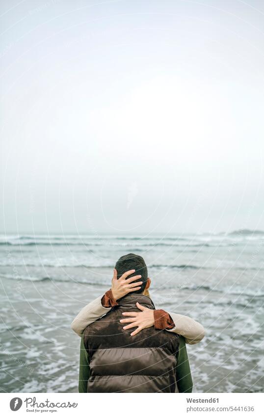Frau umarmt Mann an der Strandpromenade im Winter Paar Pärchen Paare Partnerschaft umarmen Umarmung Umarmungen Arm umlegen Meer Meere Mensch Menschen Leute