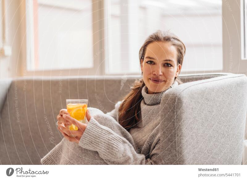 Porträt einer Frau, die auf einer Couch sitzt und ein frisches Getränk hält sitzen sitzend lächeln weiblich Frauen Erwachsener erwachsen Mensch Menschen Leute